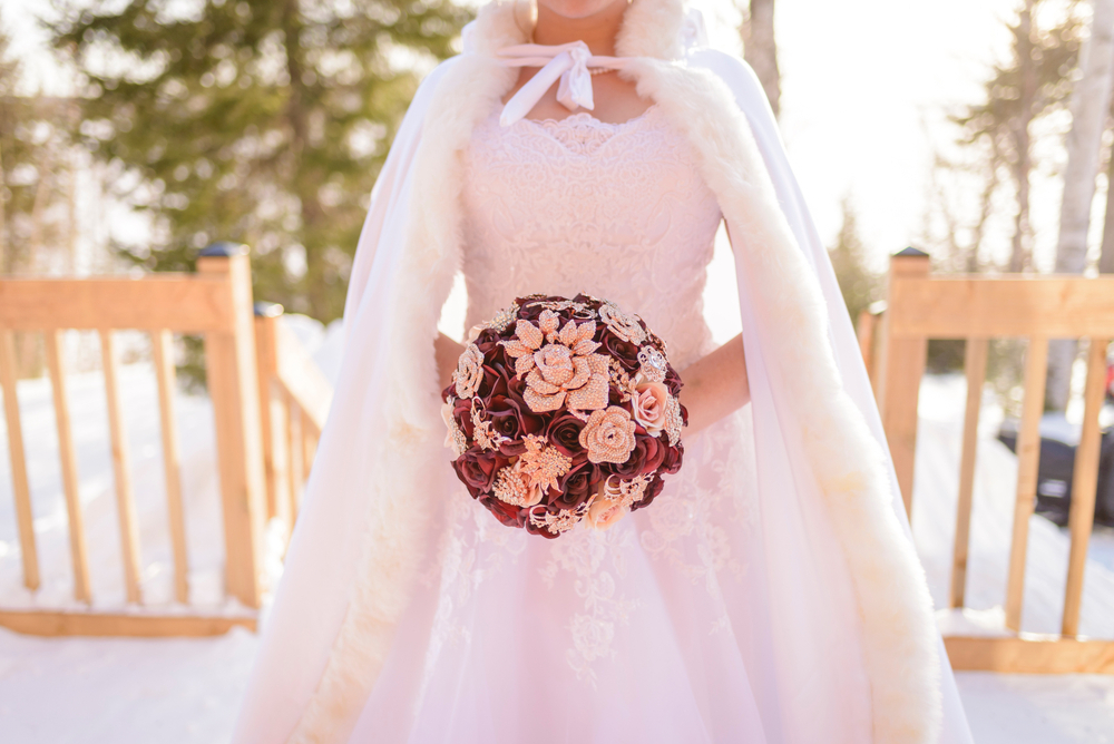 Close up of the bride with her cape holding her brooches bouquet at a winter wedding ceremony